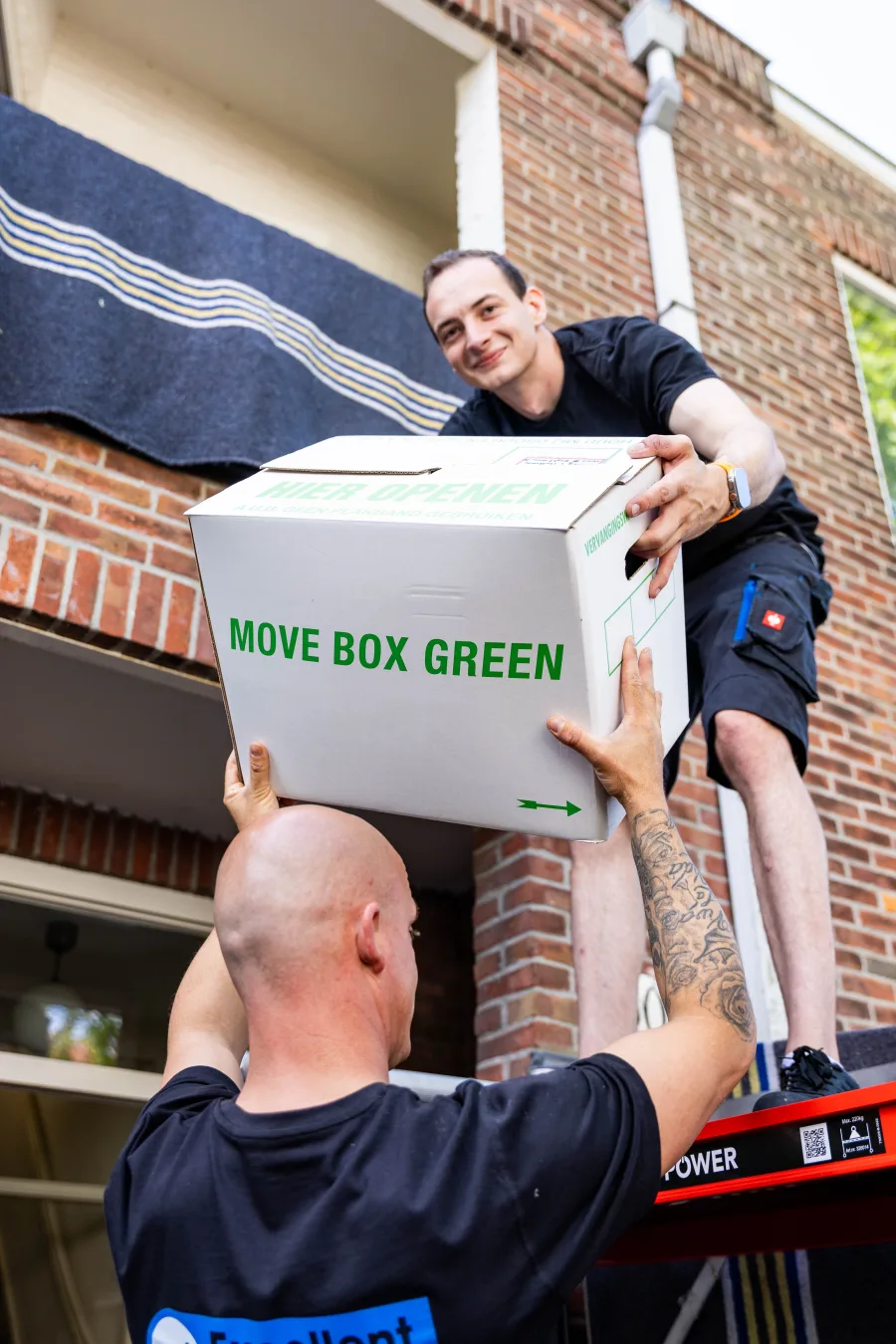 Twee verhuizers van Excellent geven een verhuisdoos over op de verhuislift tijdens een verhuizing op hoogte